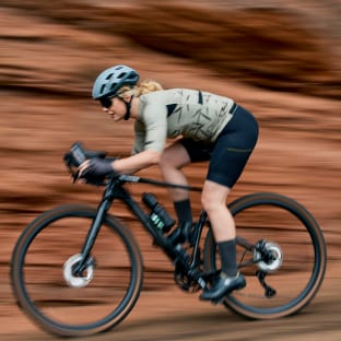 Cyclist riding a bicycle on a dirt trail with a rocky background