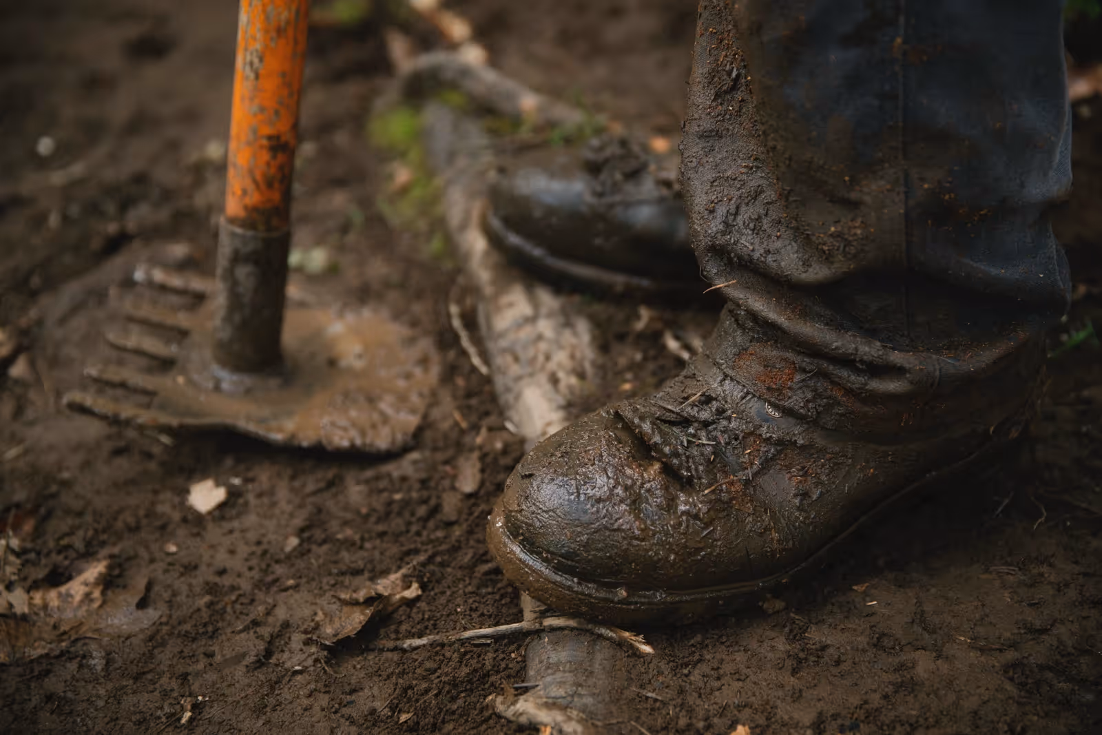 Un volontaire travaille sur le sentier, les chaussures pleines de boue.