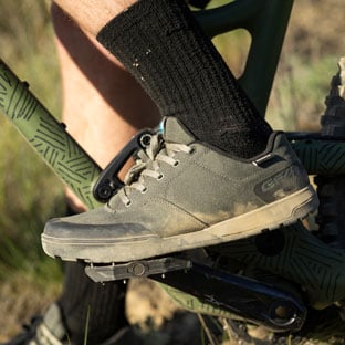 Cyclist wearing black socks and green bike shoes on a mountain bike pedal