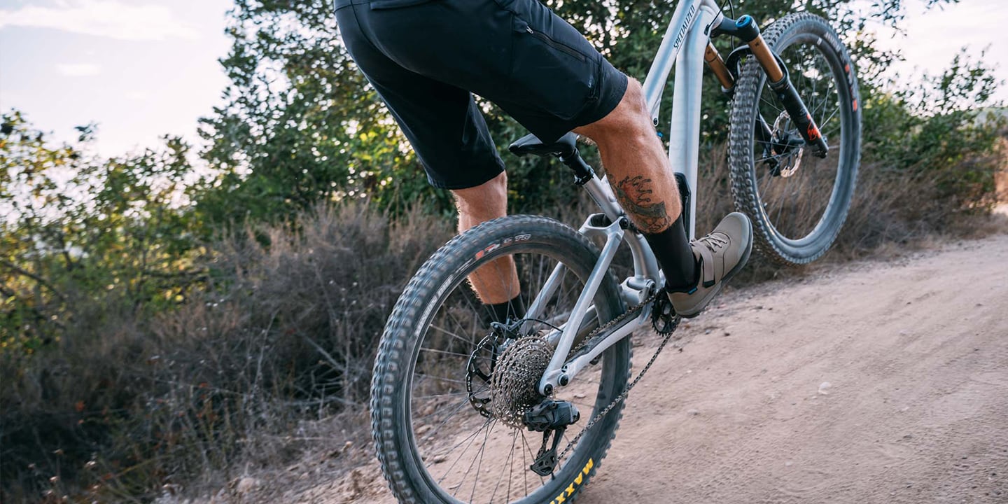 Close-up of a cyclist's foot wearing gray cycling shoes clipped into the pedal of a mountain bike