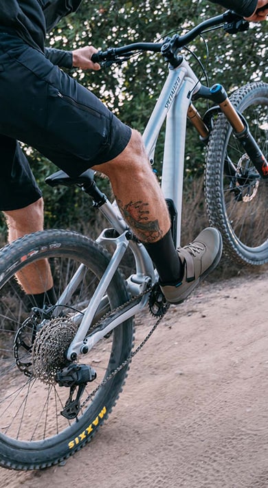 Close-up of a cyclist's foot wearing gray cycling shoes clipped into the pedal of a mountain bike