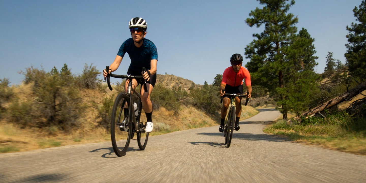Two cyclists riding on a scenic road with trees and hills in the background