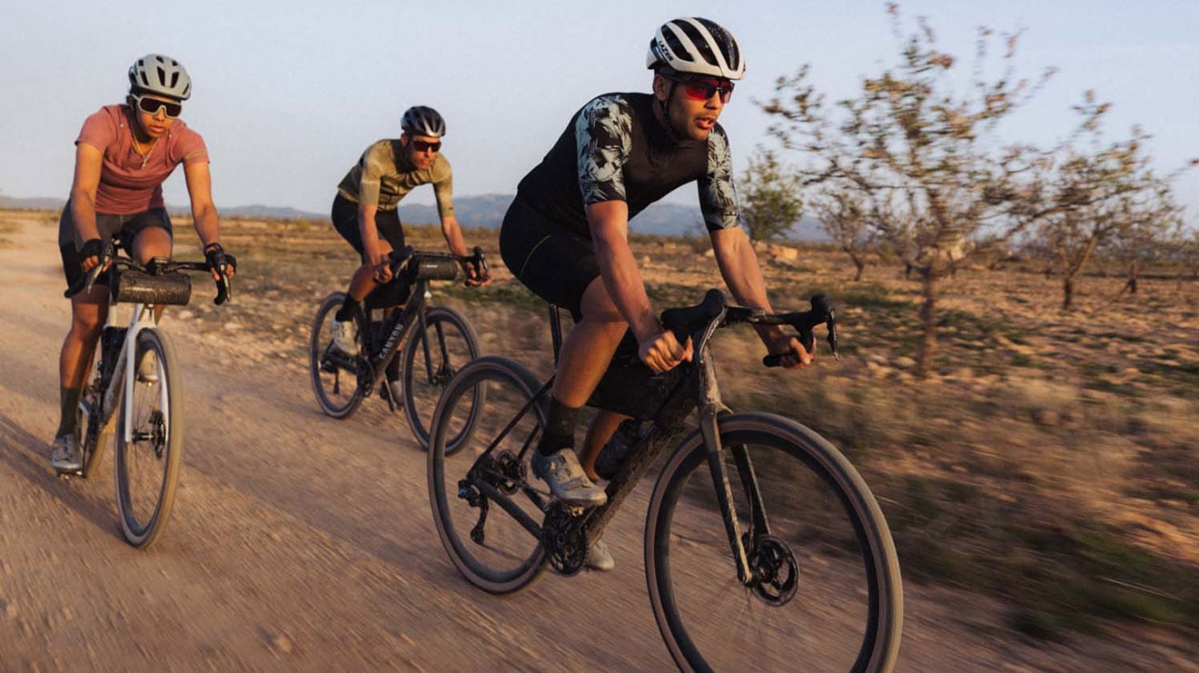 Three cyclists riding on a dirt trail in the countryside with trees in the background.