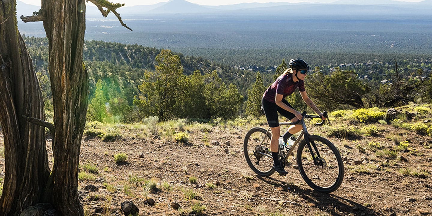 Cyclist on a mountain trail surrounded by trees and distant scenic landscape