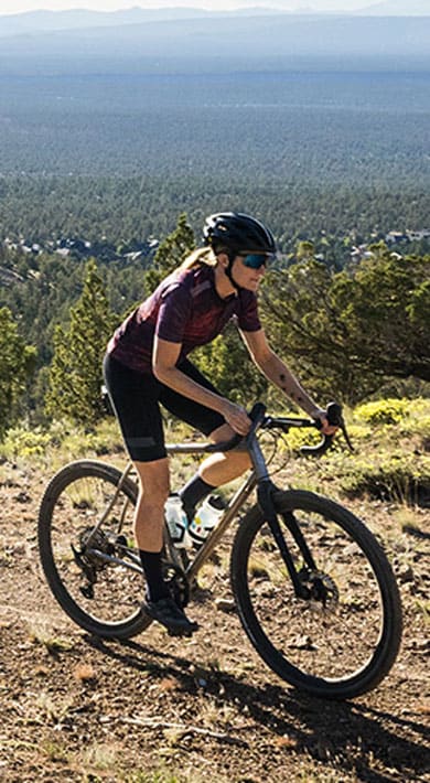 Cyclist on a mountain trail surrounded by trees and distant scenic landscape