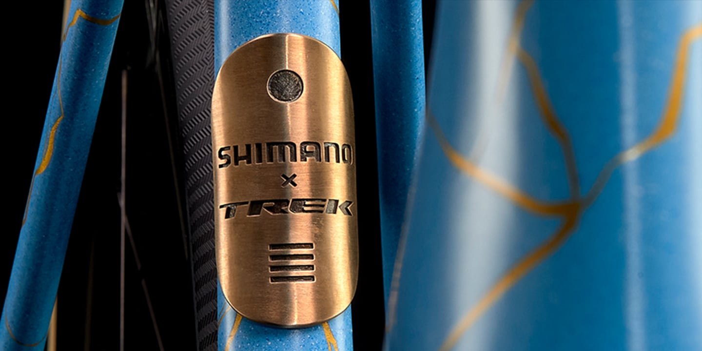 Close-up of a blue bicycle frame with a bronze Shimano x Trek badge