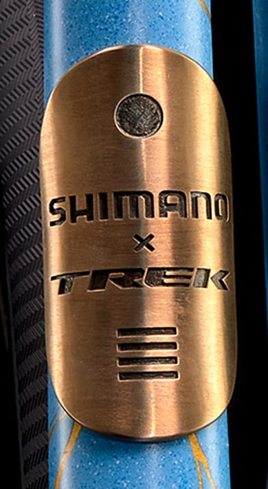 Close-up of a blue bicycle frame with a bronze Shimano x Trek badge