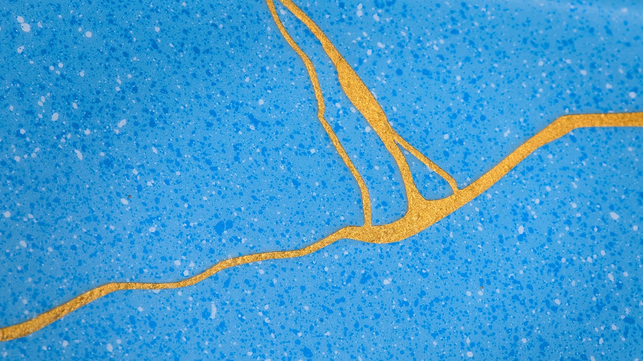 Close-up of blue speckled surface with gold abstract line pattern