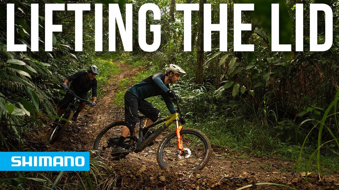 Two mountain bikers riding through a forest trail with 'Lifting the Lid' text overlay and Shimano logo