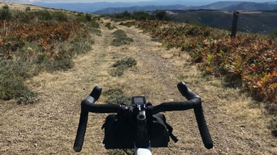 Fahrradlenker mit Blick auf einen malerischen Bergpfad unter teils bewölktem Himmel.