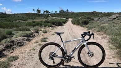 Fahrrad auf einem Schotterweg durch malerische grüne Hügel unter blauem Himmel.