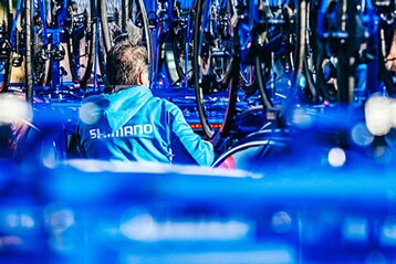 Personne en veste bleue Shimano entourée de vélos.