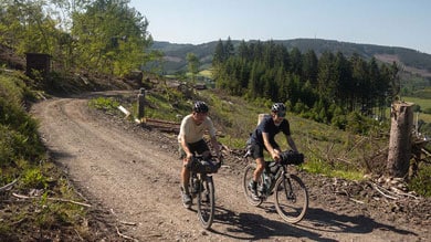 Twee fietsers rijden over een onverhard pad door een bosrijk landschap.