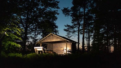 Verlicht huisje in het bos tijdens de schemering.