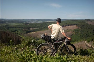 Fietser kijkt uit over een schilderachtig landschap met heuvels en bossen.