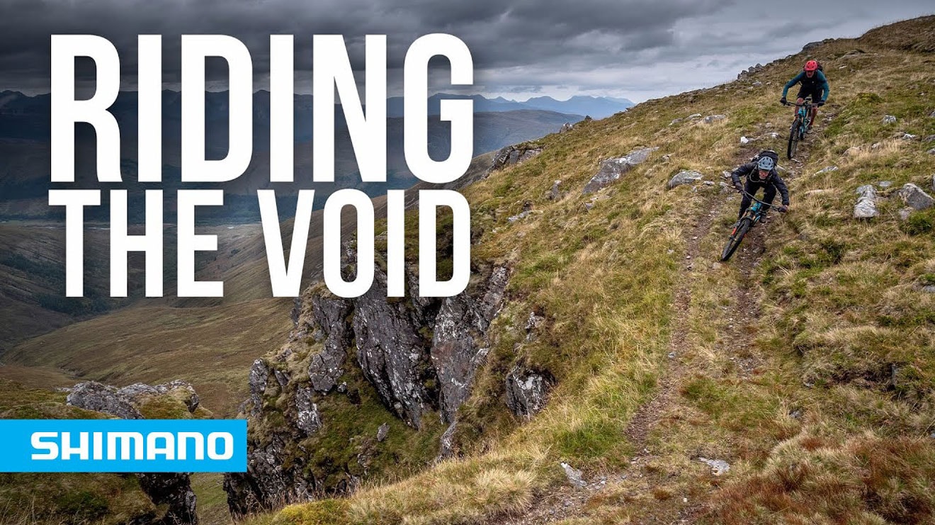 Two cyclists riding down a mountain trail with text 'Riding the Void' and Shimano logo in foreground.