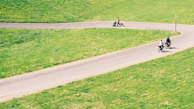 Trois personnes sur un sentier dans un champ herbeux, deux à vélo, une poussant une poussette.