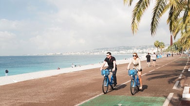 Deux personnes faisant du vélo près de la plage par une journée ensoleillée avec des palmiers.