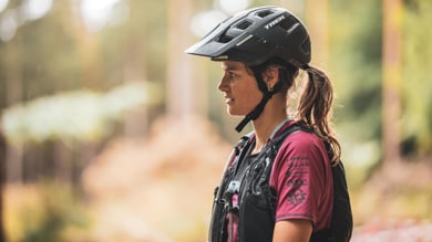 Woman in a helmet and cycling gear standing outdoors in a forested area