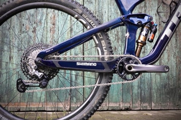 Close-up of a bike's Shimano gear mechanism and rear suspension against a wooden background.