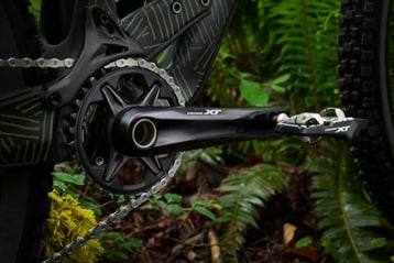 Close-up view of Shimano Deore XT bike crankset in a forest setting