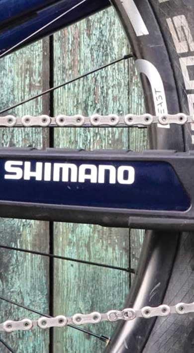 Close-up of Shimano bike chain and gears against a rustic wooden background