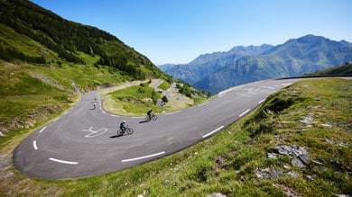 Cyclists riding on a mountainous winding road under a clear blue sky