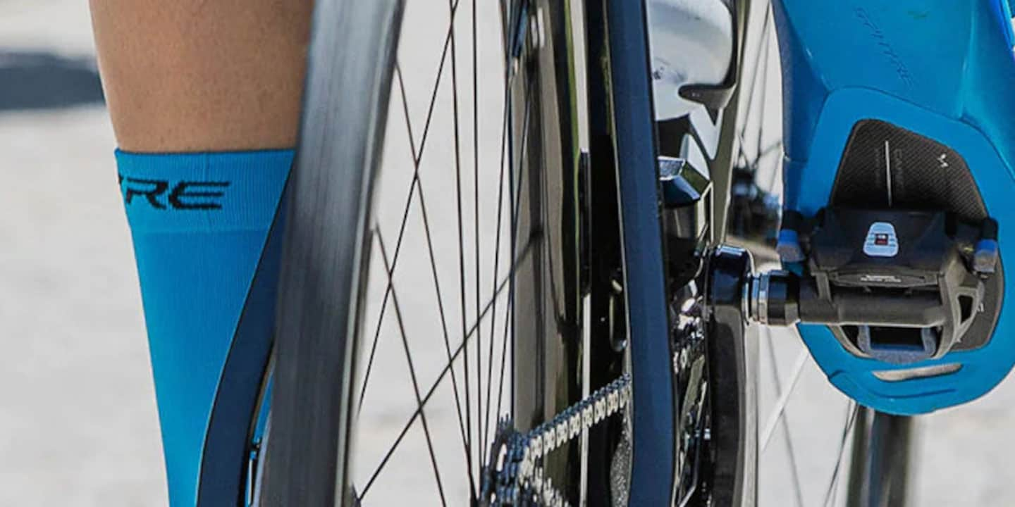 Close-up of a cyclist's foot on a pedal with blue socks and bike gears in view