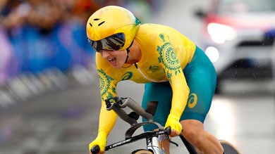 Cyclist in yellow suit and helmet racing on a road bike during a competition.