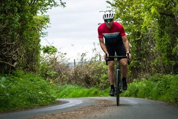 Cyclist in red and black outfit riding on a rural road