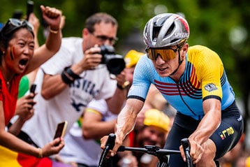 Cyclist in colorful jersey racing, surrounded by cheering fans.