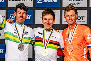 Three cyclists on podium with medals at a cycling event.