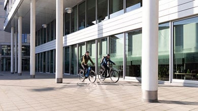 Zwei Radfahrer fahren mit ihren Fahrrädern vor einem modernen Gebäude.