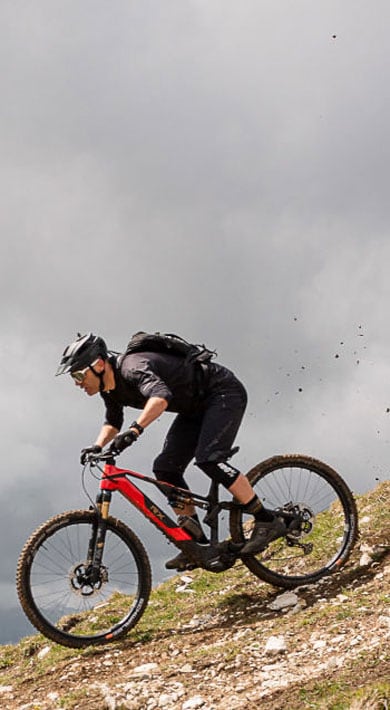 Zwei Mountainbiker fahren einen felsigen Abhang unter wolkenverhangenem Himmel hinunter.