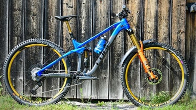 Blaues und orangefarbenes Mountainbike an einer Holzwand.