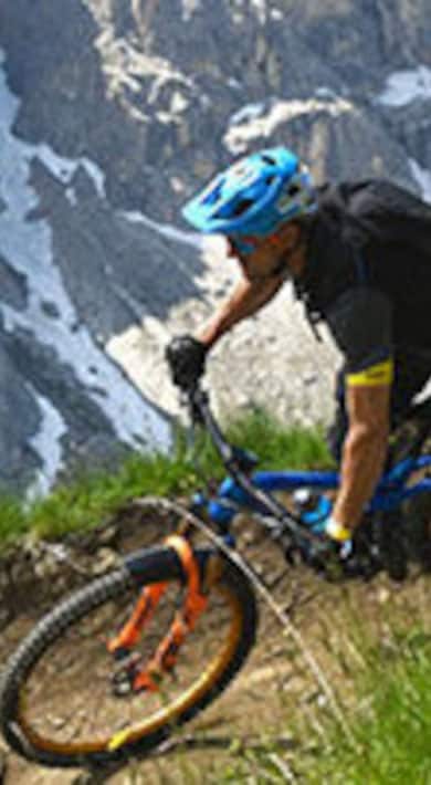 Mountainbiker fährt einen felsigen Pfad mit Klippen im Hintergrund hinunter.