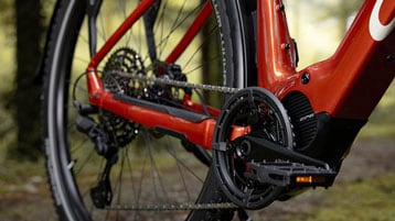 Close-up of red electric bike drivetrain and pedals on a forest trail