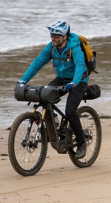 Two cyclists in colorful jackets riding on a grassy trail.