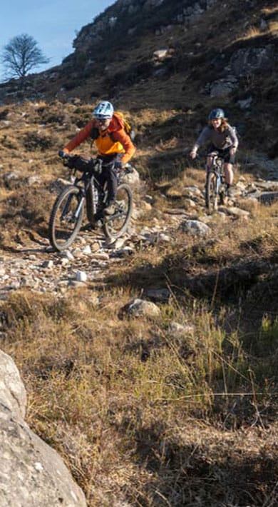 Two cyclists riding on a rocky trail through a mountainous landscape