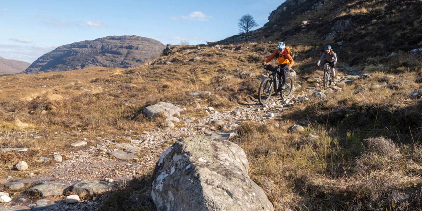 Two cyclists riding on a rocky trail through a mountainous landscape