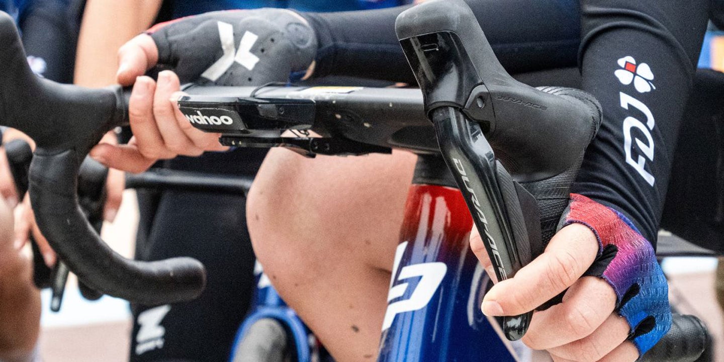 Close-up of cyclists' hands on handlebars, wearing gloves and FDJ branded clothing.