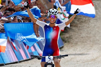 Cyclist celebrates victory at race finish line, surrounded by cheering crowd with flags