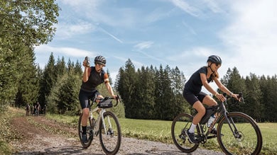 Radfahrer fahren auf einem ländlichen Weg mit Bäumen und blauem Himmel im Hintergrund.