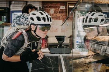 Radfahrer mit Helm und Sonnenbrille schaut in die Auslage einer Bäckerei.