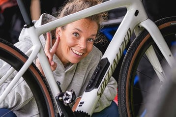 Lächelnde Person zeigt das Peace-Zeichen neben einem geparkten Fahrrad.