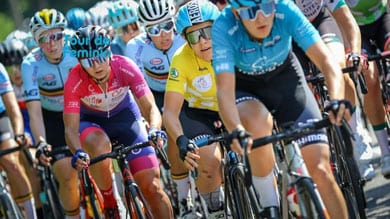 Radfahrerinnen treten beim Tour de Feminin-Rennen an, mit einer Fahrerin im gelben Trikot im Zentrum, umgeben von Konkurrentinnen in blauen und roten Trikots, alle mit Helmen und Sonnenbrillen.