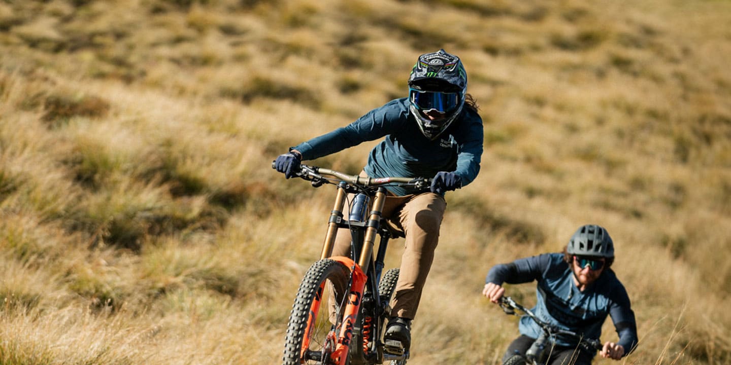 Two cyclists mountain biking downhill on a grassy terrain.