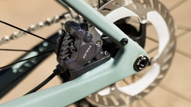 Close-up of a GRX bicycle brake caliper and rotor on a mint green bike