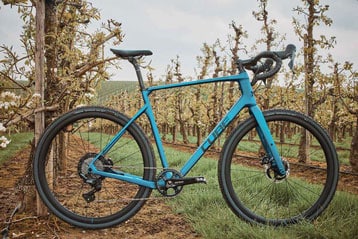 Blaues Rennrad in einer Obstplantage mit blühenden Bäumen.