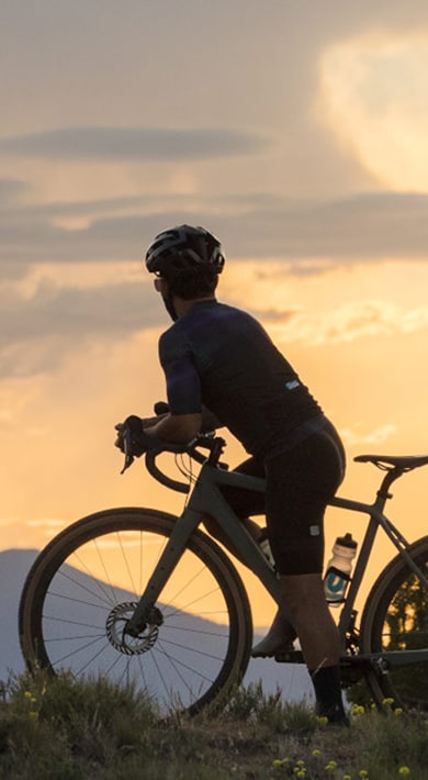Radfahrer auf einem Trail bei Sonnenuntergang mit Bergen im Hintergrund.